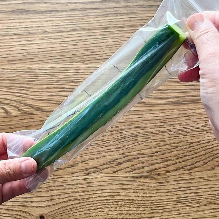 手で持ったビニール袋に入ったキュウリ。木目調の背景。