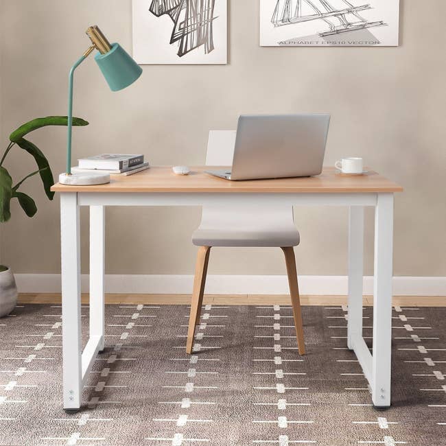 Minimalist workspace with a woody desk, laptop, greenish lamp, and seat connected a patterned rug. Decor includes modern creation and a plant