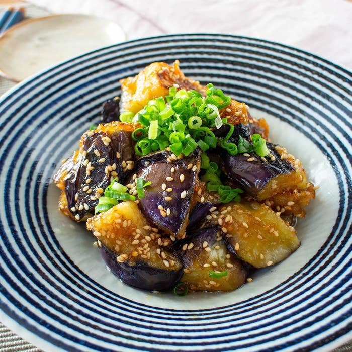 ごまを振りかけたナスの揚げ物が盛られた皿。上にネギが飾られています。
