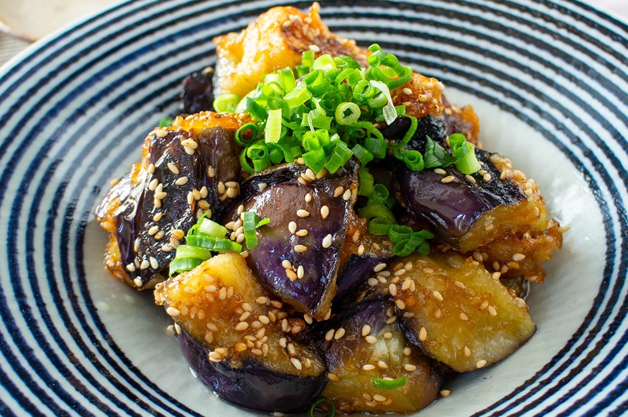 皿に盛られたナスの炒め物。ゴマとネギがトッピングされ、食欲をそそる見た目です。