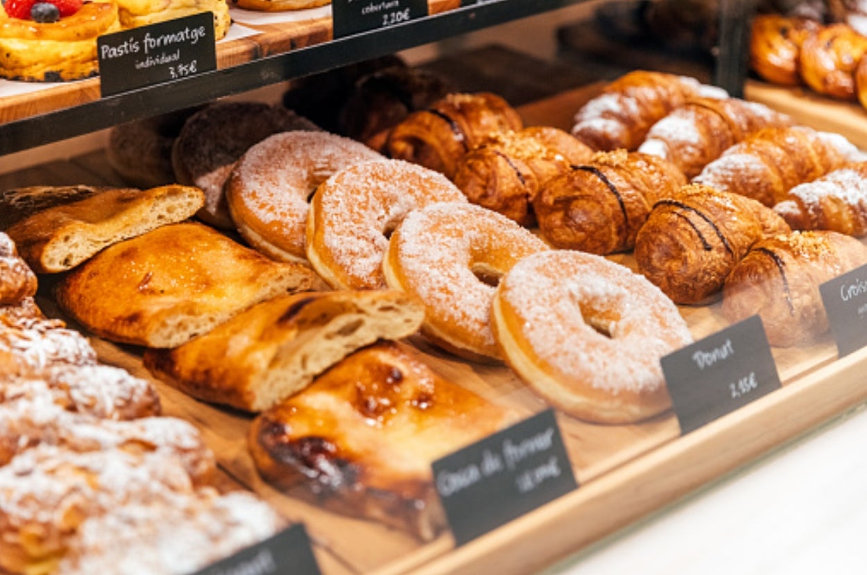 A display case with various pastries including donuts, croissants, and turnovers. Each item is labeled with a price tag