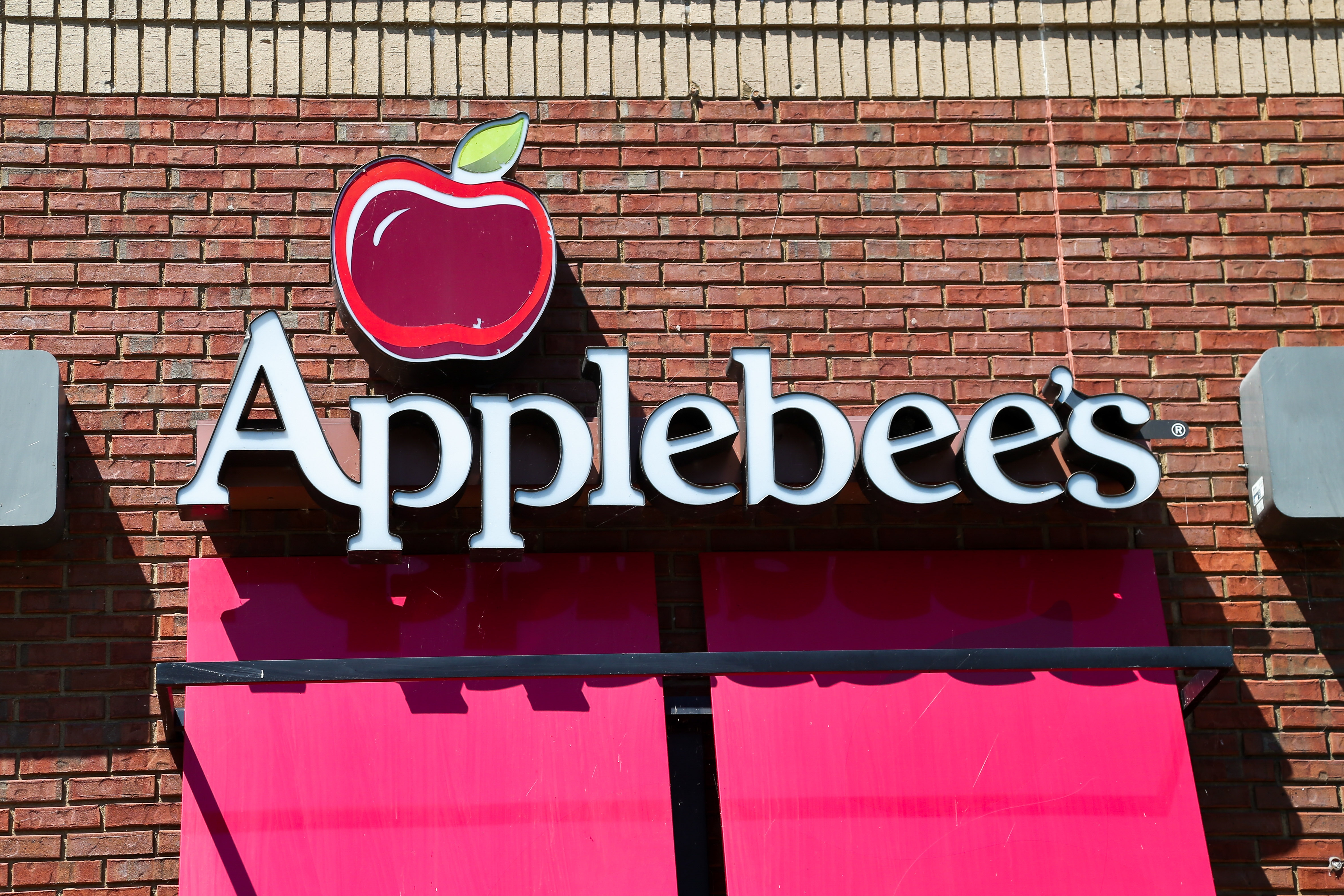 Applebee's restaurant sign with a red apple logo, mounted on a brick wall