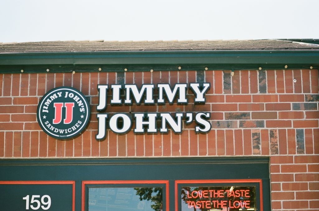 Jimmy John's brick storefront with signage and neon "Love the taste, taste the love" text in window