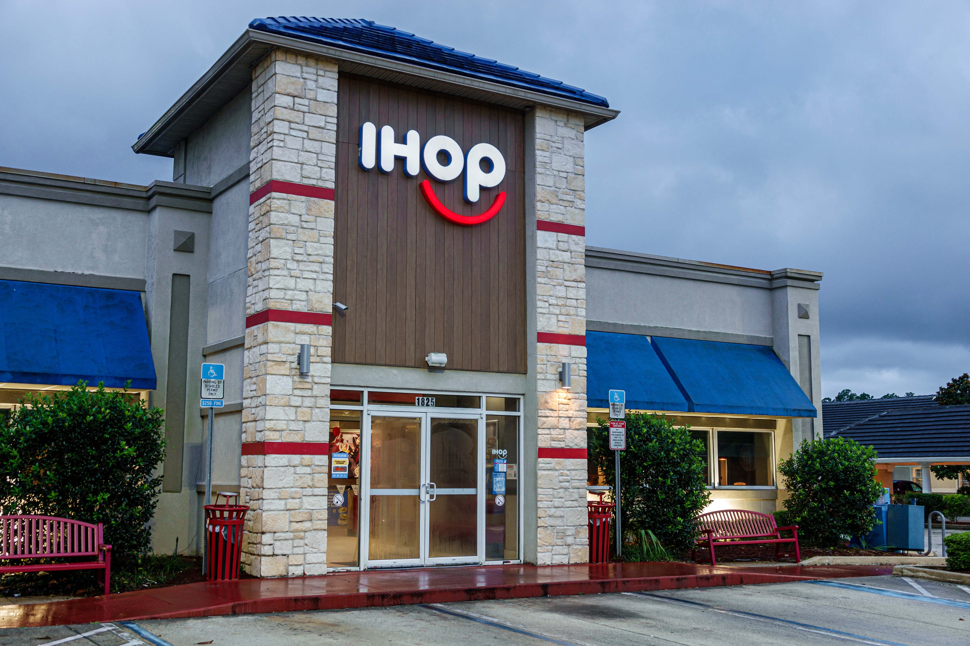 Exterior of an IHOP restaurant with a prominent logo, showing the building entrance and surrounding greenery