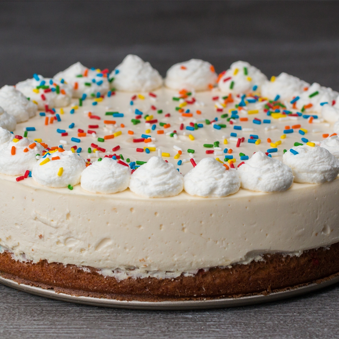 A cheesecake with whipped cream dollops around the edge and colorful sprinkles on top