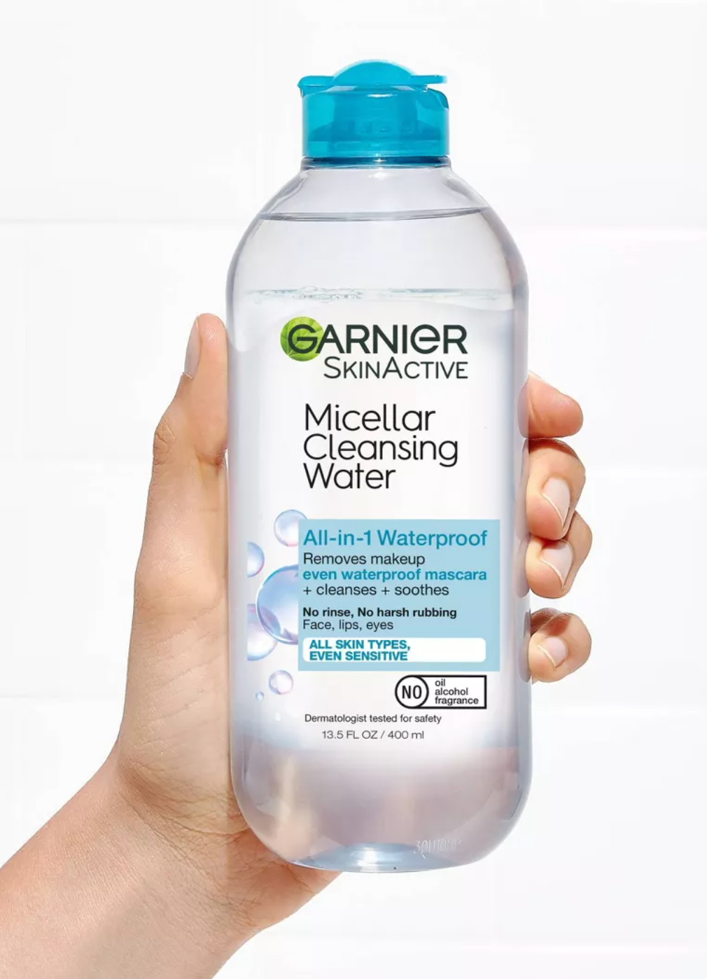 Tangan memegang botol air pembersih micellar garnier, diberi label sebagai penghapus makeup tahan air all-in-1 untuk semua jenis kulit, termasuk sensitif