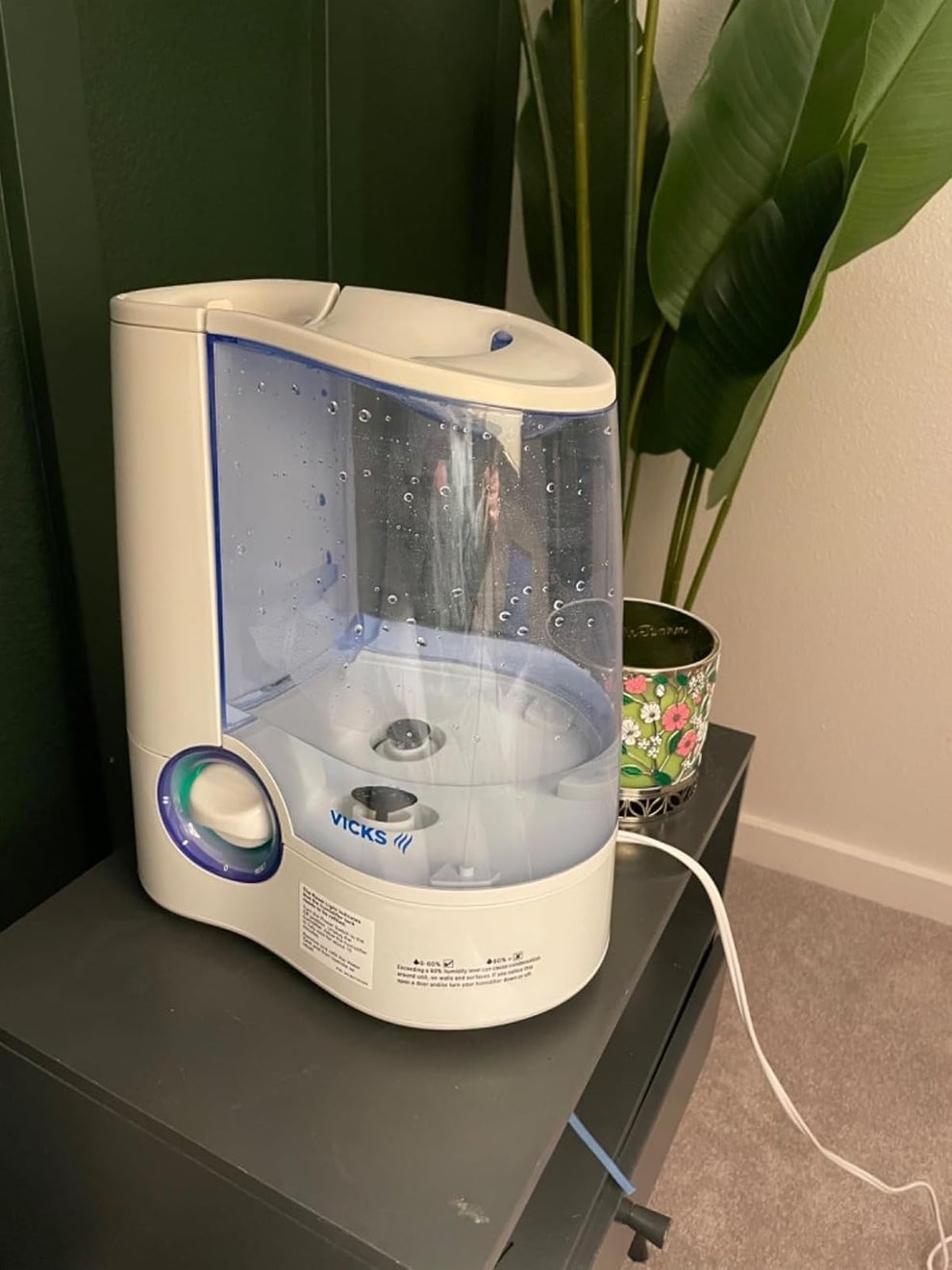 Vicks humidifier on a dark side table with a plant nearby, showing water droplets inside the tank