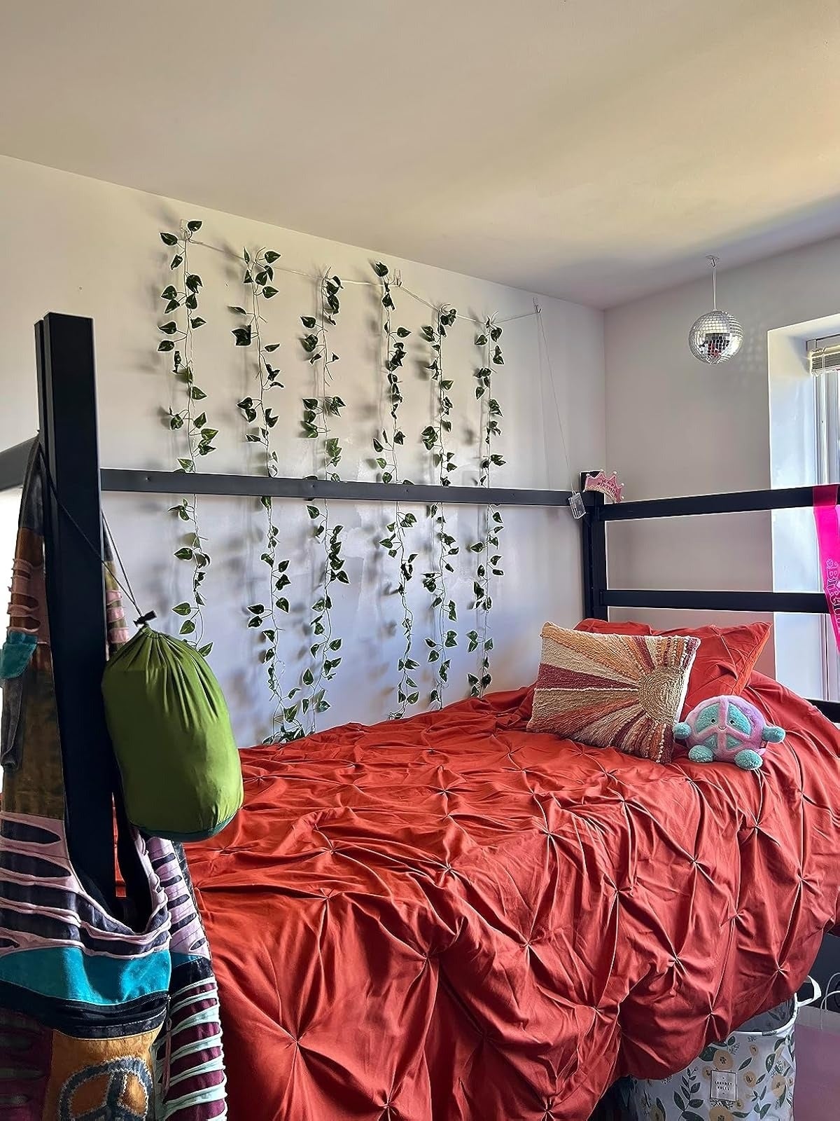 Loft furniture  with reddish  bedding, hanging plants connected  the wall, and a tiny  disco shot  above