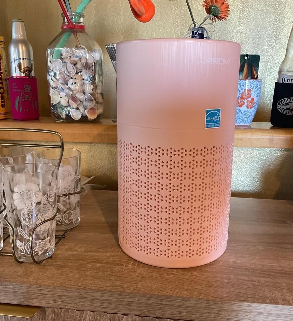 Pink air purifier on a wooden surface, surrounded by glassware and decorative items in a cozy home setting