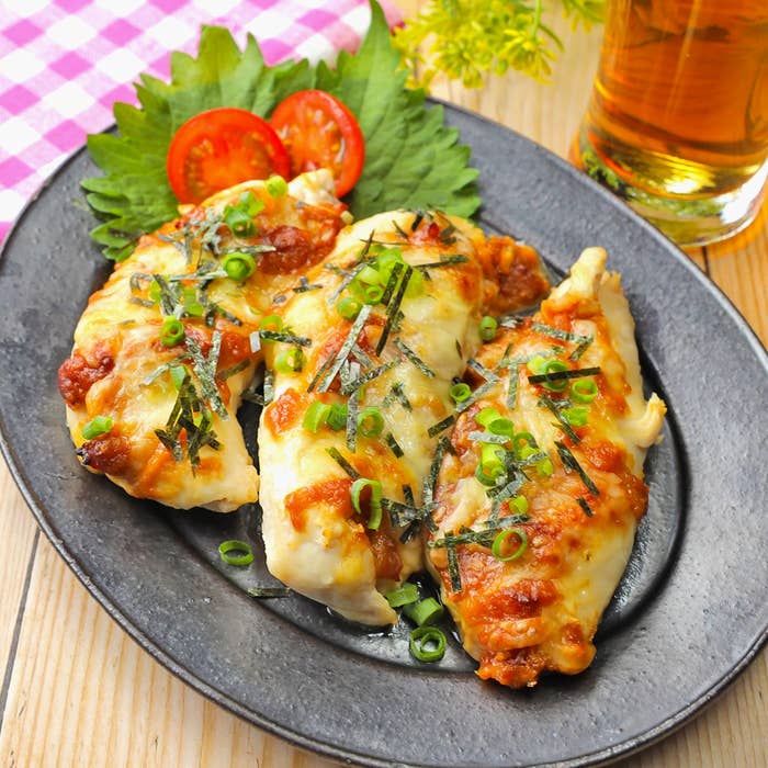 皿に盛られたチーズと海苔がトッピングされた鶏肉料理。飾りとしてトマトと葉野菜、小さなグラスの飲み物が背景にある。