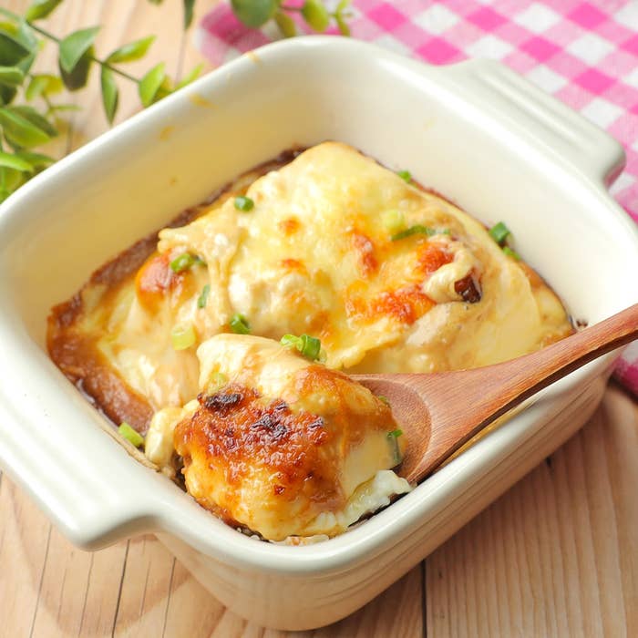 クリーミーなチーズが溶けた焼き豆腐に、木製スプーンが添えられている。上にネギのトッピングがある。