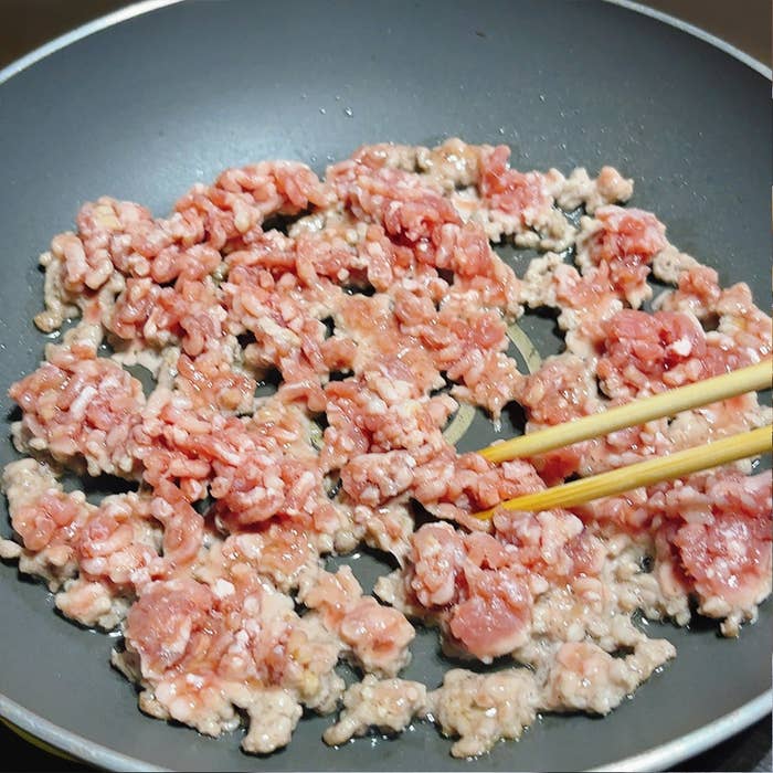フライパンで炒められているミンチ肉を箸で混ぜている様子。