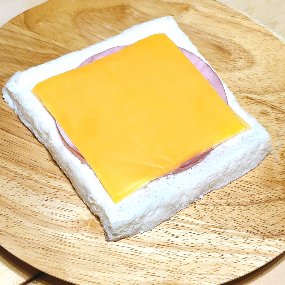 木製プレートにハムとチーズをのせた食パンの開いたサンドイッチ。