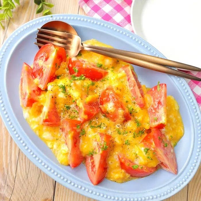 トマトと卵がのったオムレツ風の料理が楕円形の皿に盛られ、カトラリーが添えられている。