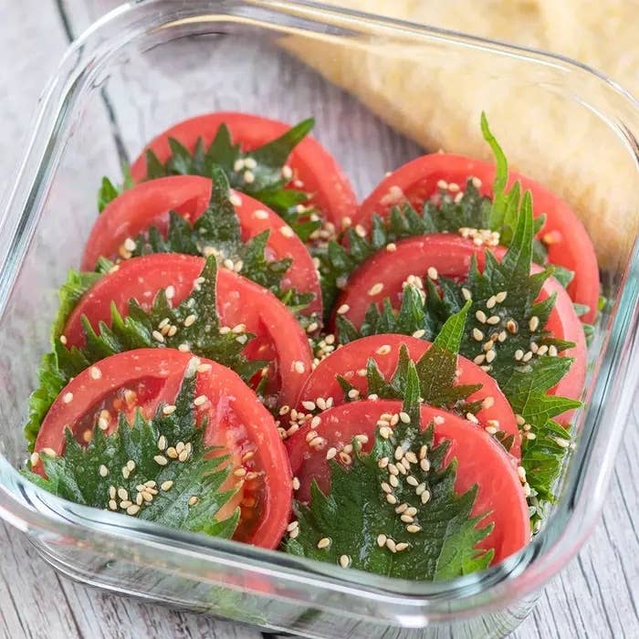ガラス容器に盛り付けられたトマトと大葉のサラダ。ごまとパンが添えられている。