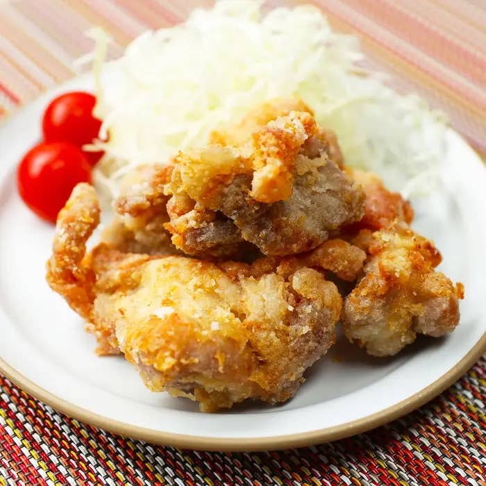 揚げた鶏のからあげが白いお皿に載っており、付け合わせに千切りキャベツとチェリートマトが添えられています。