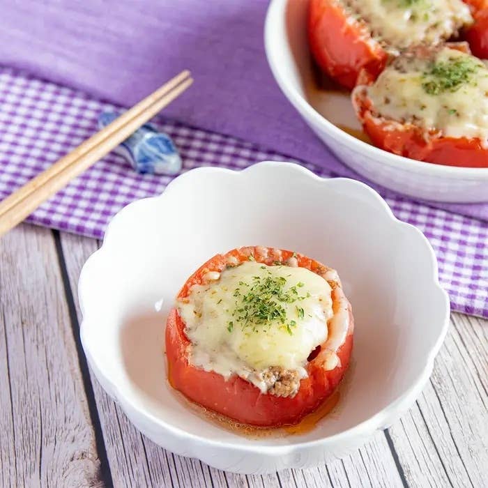 皿に盛られた肉詰めトマトのチーズ焼き。テーブルに箸ともう一皿の料理が見える。