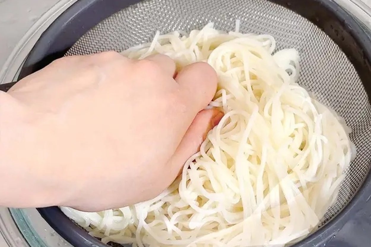 手がざるにある麺をすすいでいる様子。調理シーンを示す。