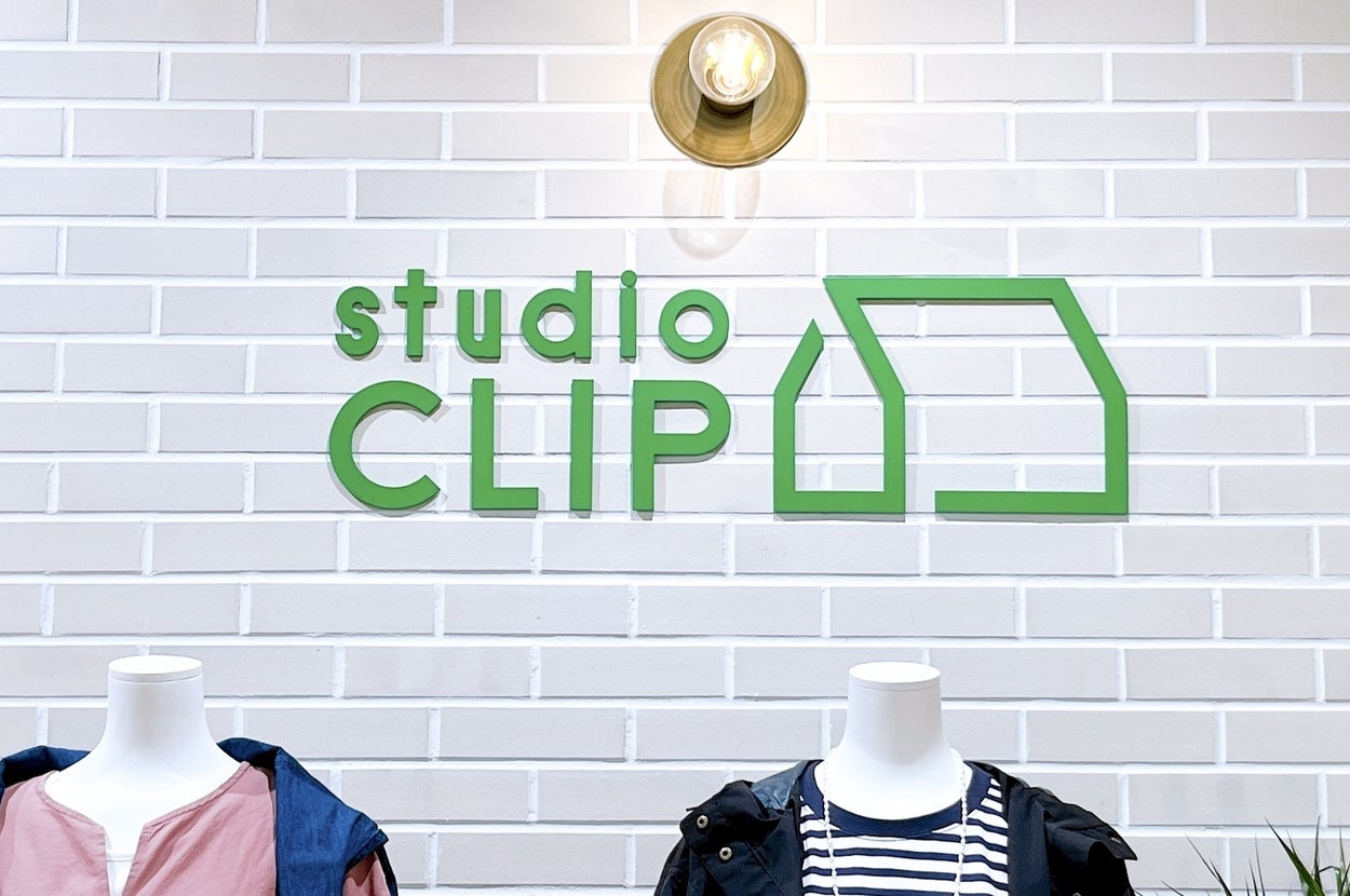 白いレンガの壁に「studio CLIP」のロゴがあり、2体のマネキンが服を着ています。
