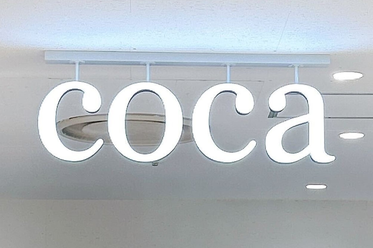 店内に「coca」と書かれたネオンサインが天井に設置され、周囲に洋服が陳列されている。