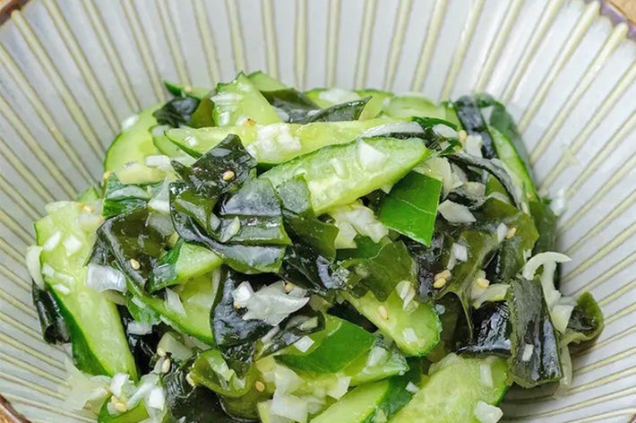 きゅうりと海藻のサラダが皿に盛られている。白ゴマと切り刻んだ野菜がトッピングされている。