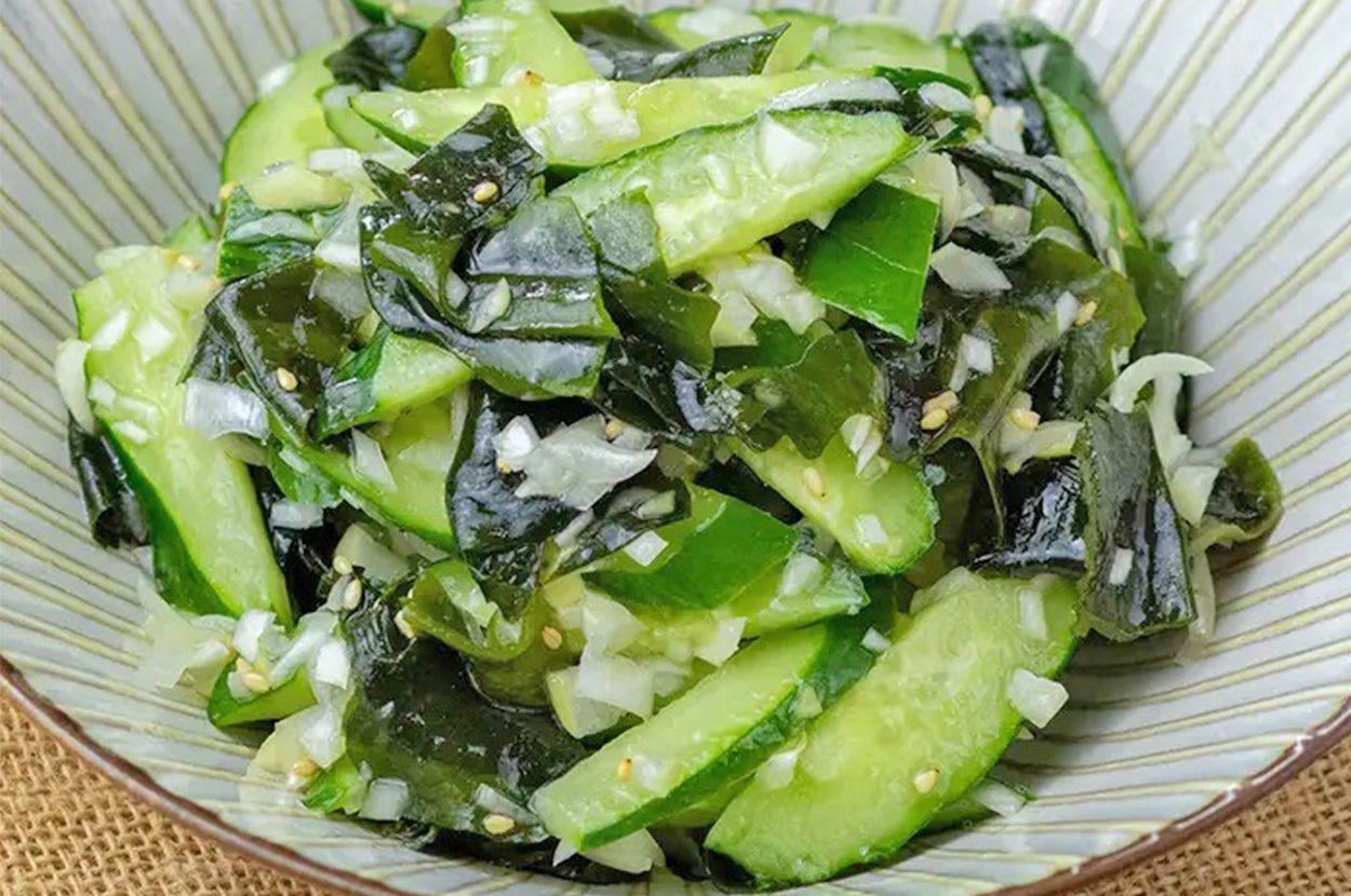 きゅうりと海藻のサラダが皿に盛られている。白ゴマと切り刻んだ野菜がトッピングされている。