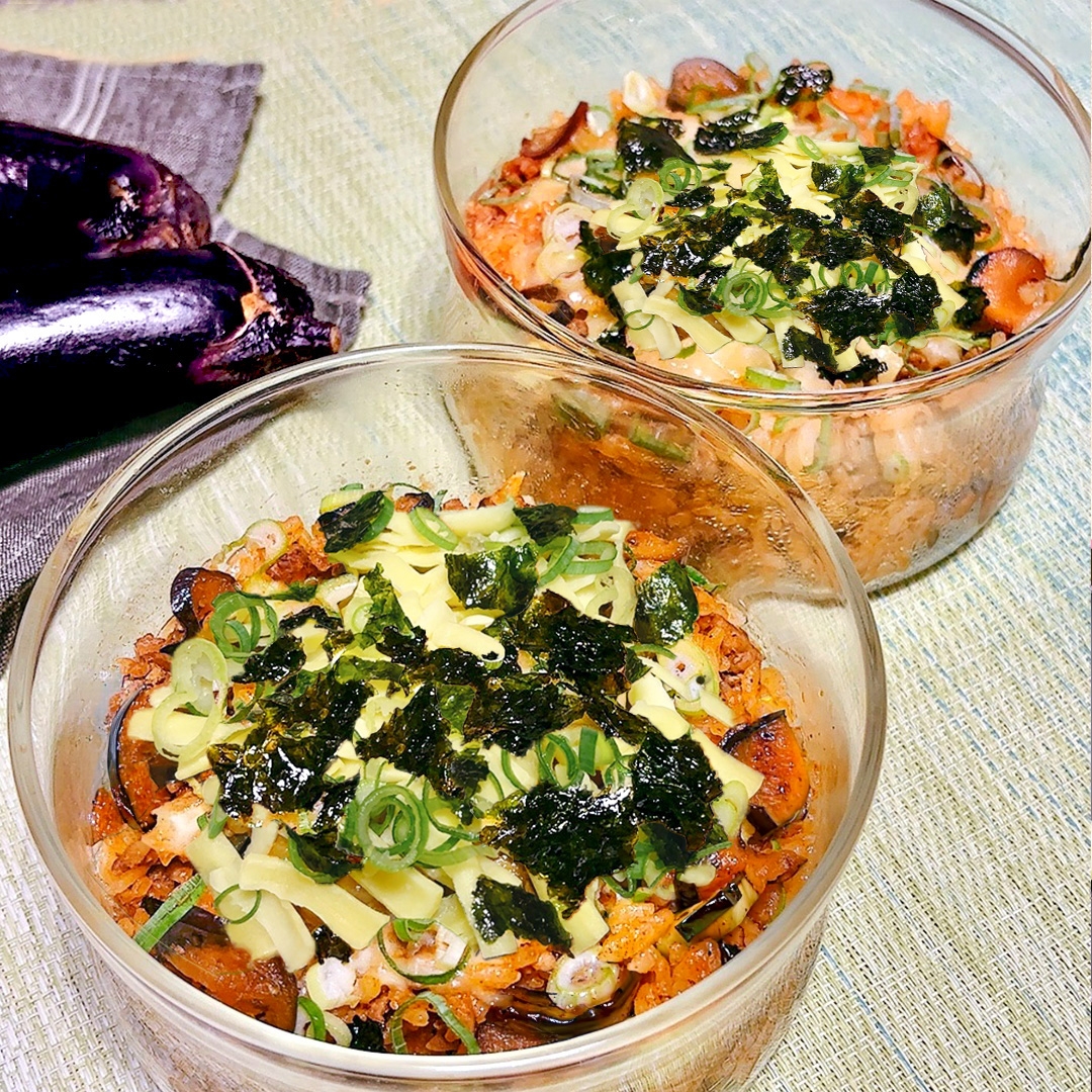 2つのガラスボウルに盛り付けられたナスと海苔が添えられたライス料理。机にはナスも置かれている。