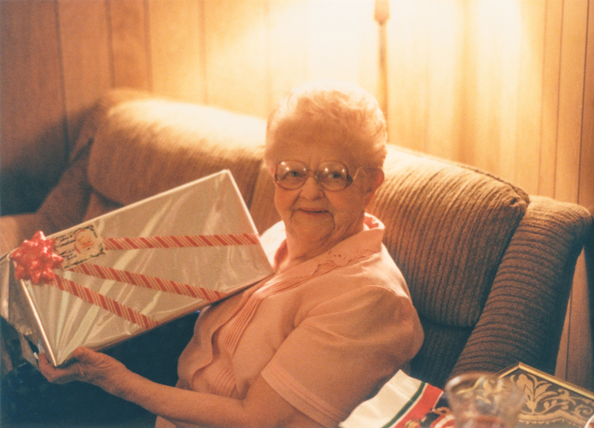 Eldre kvinne som sitter på en sofa, smiler og holder en innpakket gave med en bue, skaper en gledelig og varm atmosfære
