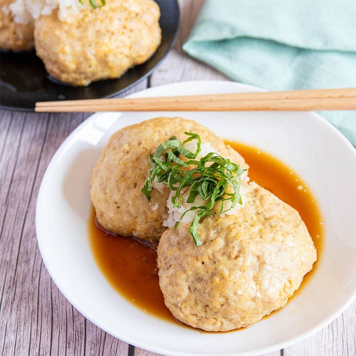 白い皿に盛られた豆腐ハンバーグ、上に大根おろしと刻んだ大葉がのっている。横に箸が置かれた和風料理。
