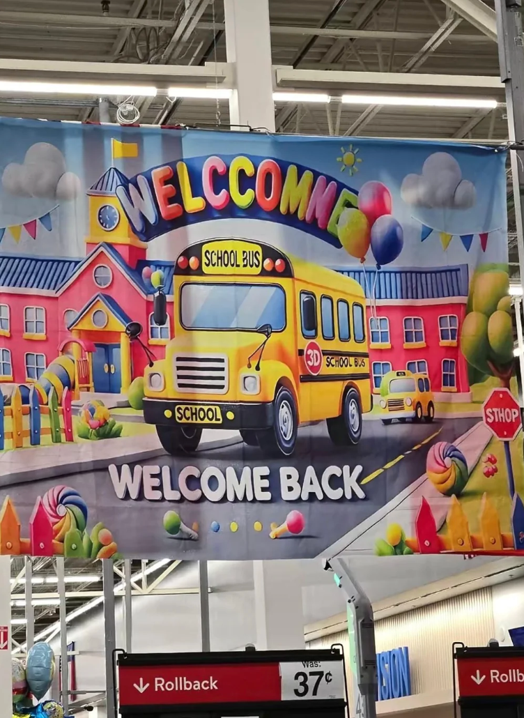 Colorful "Welcome Back" banner featuring a schoolhouse  autobus  and festive decorations; displayed supra  a store   aisle with rollback prices