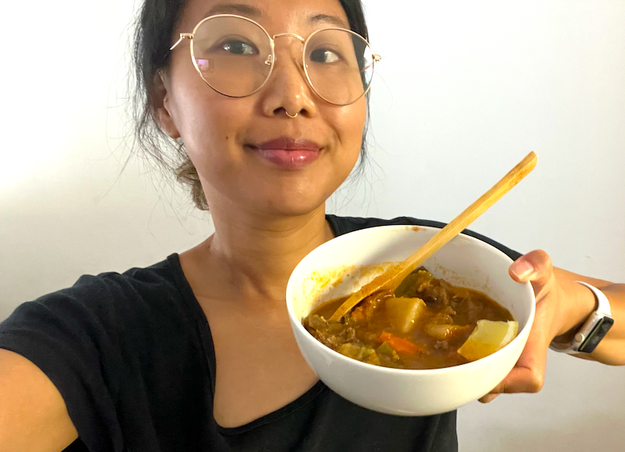 Person holding a bowl of hearty soup with visible vegetables, smiling at the camera