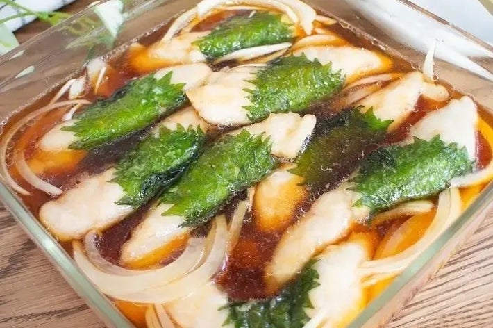 ガラスの容器に入った料理。魚の切り身と玉ねぎ、緑の葉がタレに浸されている。