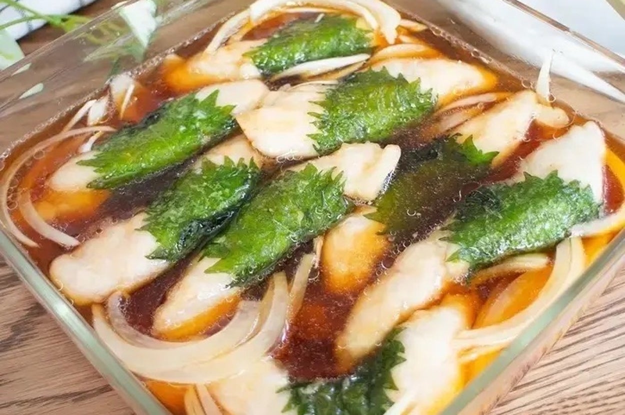 ガラスの容器に入った料理。魚の切り身と玉ねぎ、緑の葉がタレに浸されている。