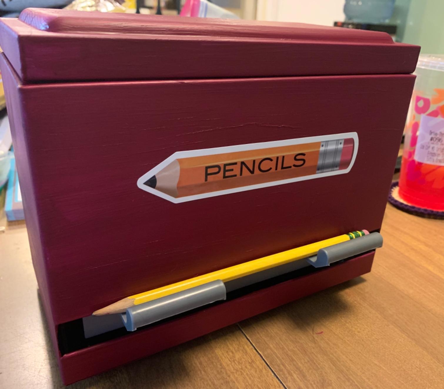 Wooden pencil holder box with a pencil graphic labeled "PENCILS" on its side, holding a yellow pencil on a desk