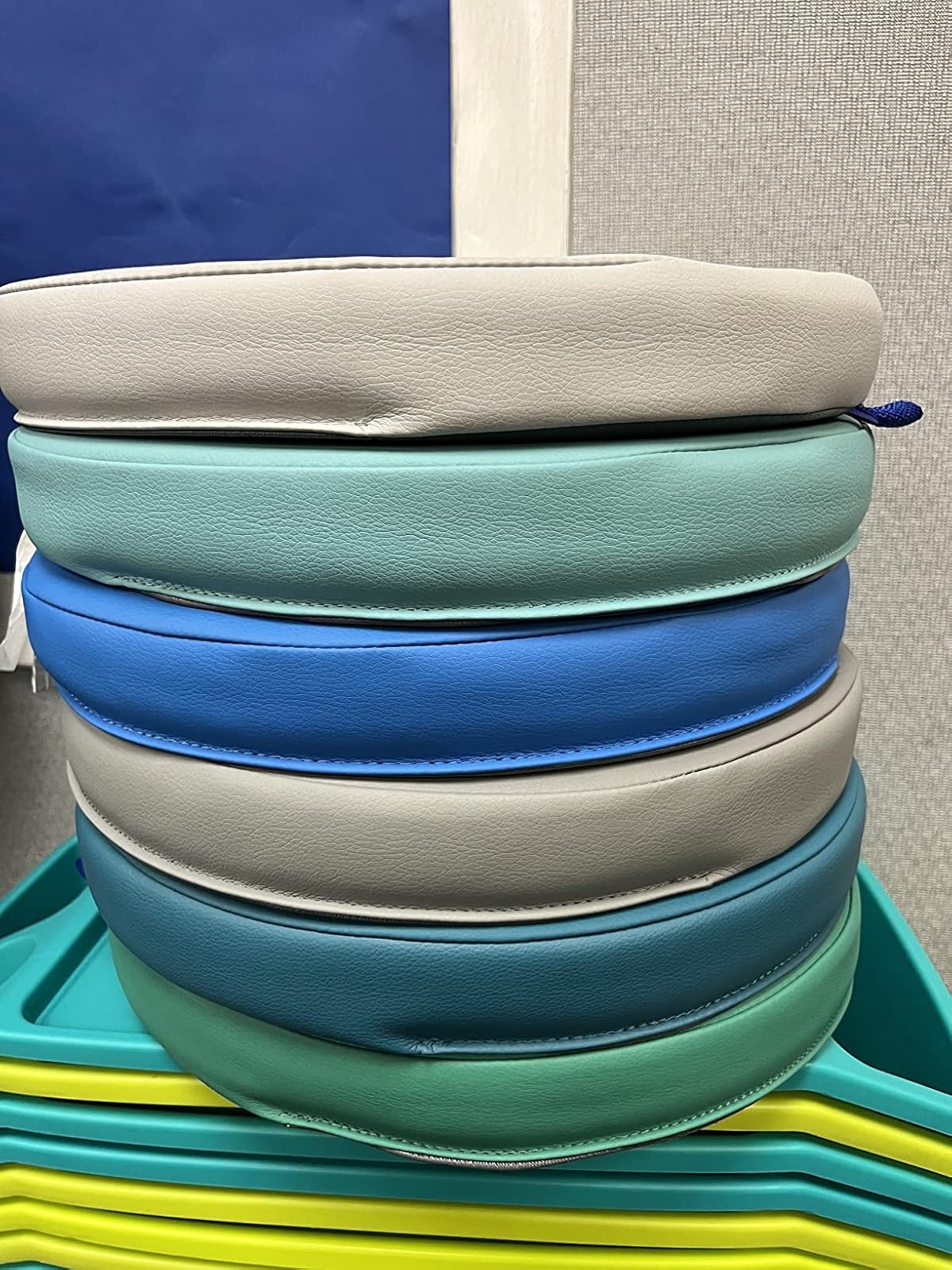 Stack of round seat cushions in various shades, arranged on a brightly colored shelf