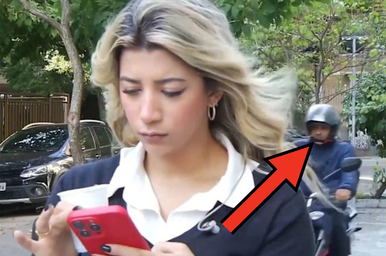 女性がスマートフォンを見ながら歩いている。後ろにバイクの乗り物が通り過ぎている。