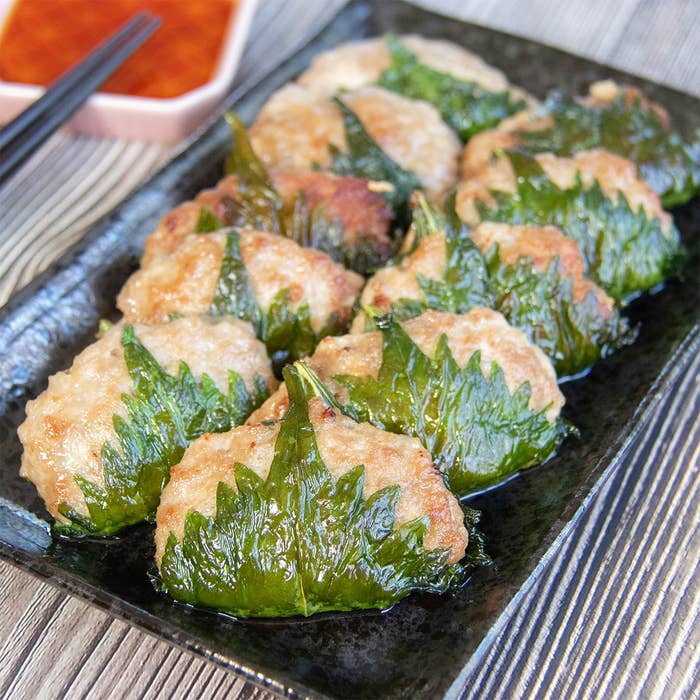 大葉で肉だねを包んで焼いた大葉ギョーザが黒い皿に並んで置かれている。横に酢じょうゆが入った小さな皿と黒い箸が見える。