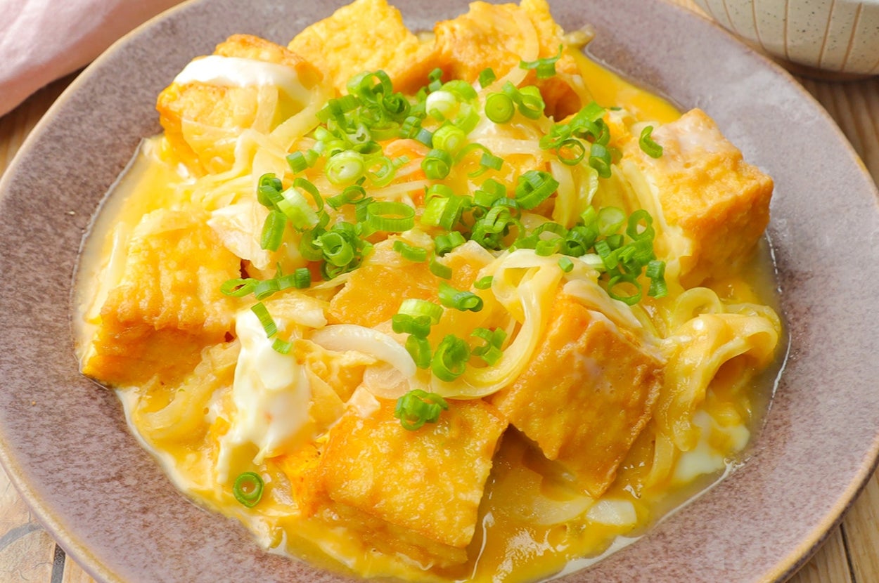 豆腐の卵とじは、細ねぎがトッピングされ、木製のテーブルに置かれたお皿に盛り付けられています。