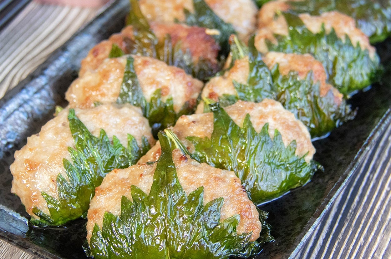 大葉で肉だねを包んで焼いた大葉ギョーザが黒い皿に並んで置かれている。横に酢じょうゆが入った小さな皿と黒い箸が見える。