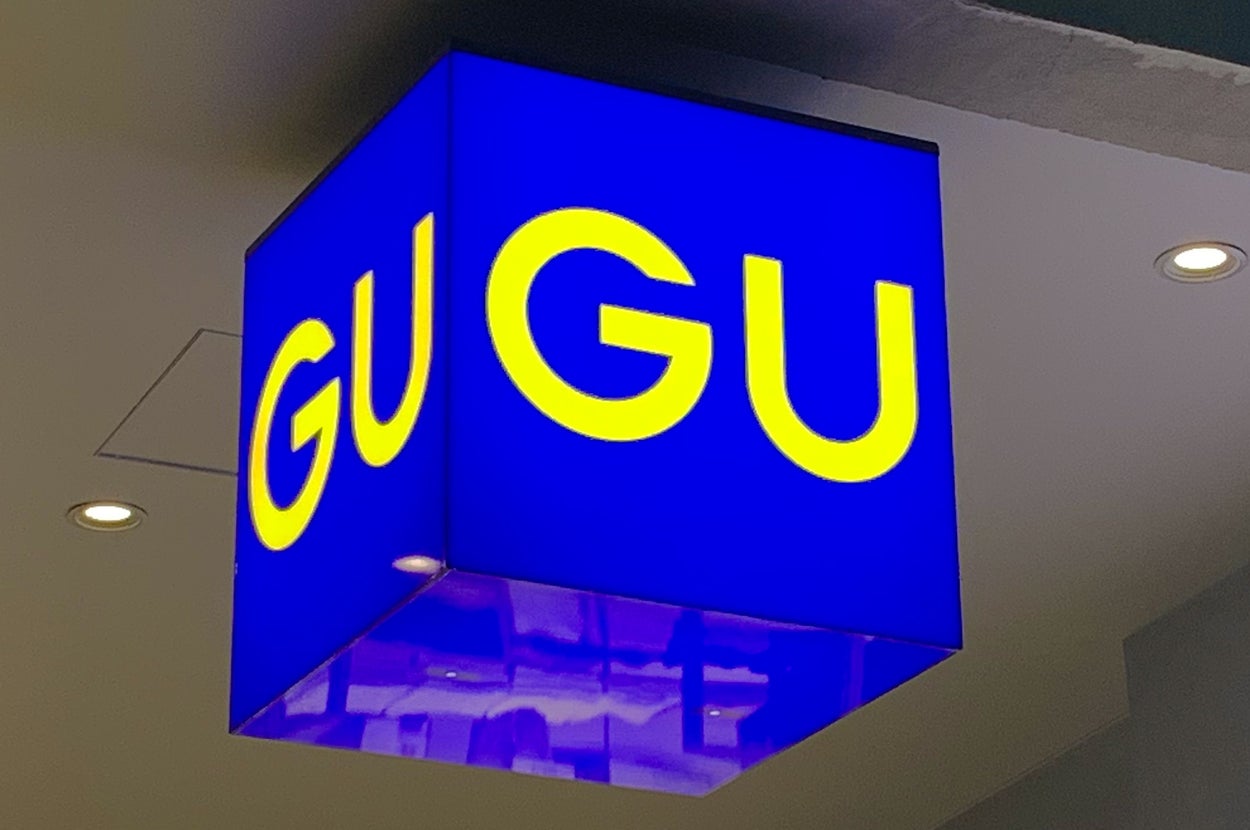Sign with "GU GU" in bold letters on a cube, illuminated and suspended indoors