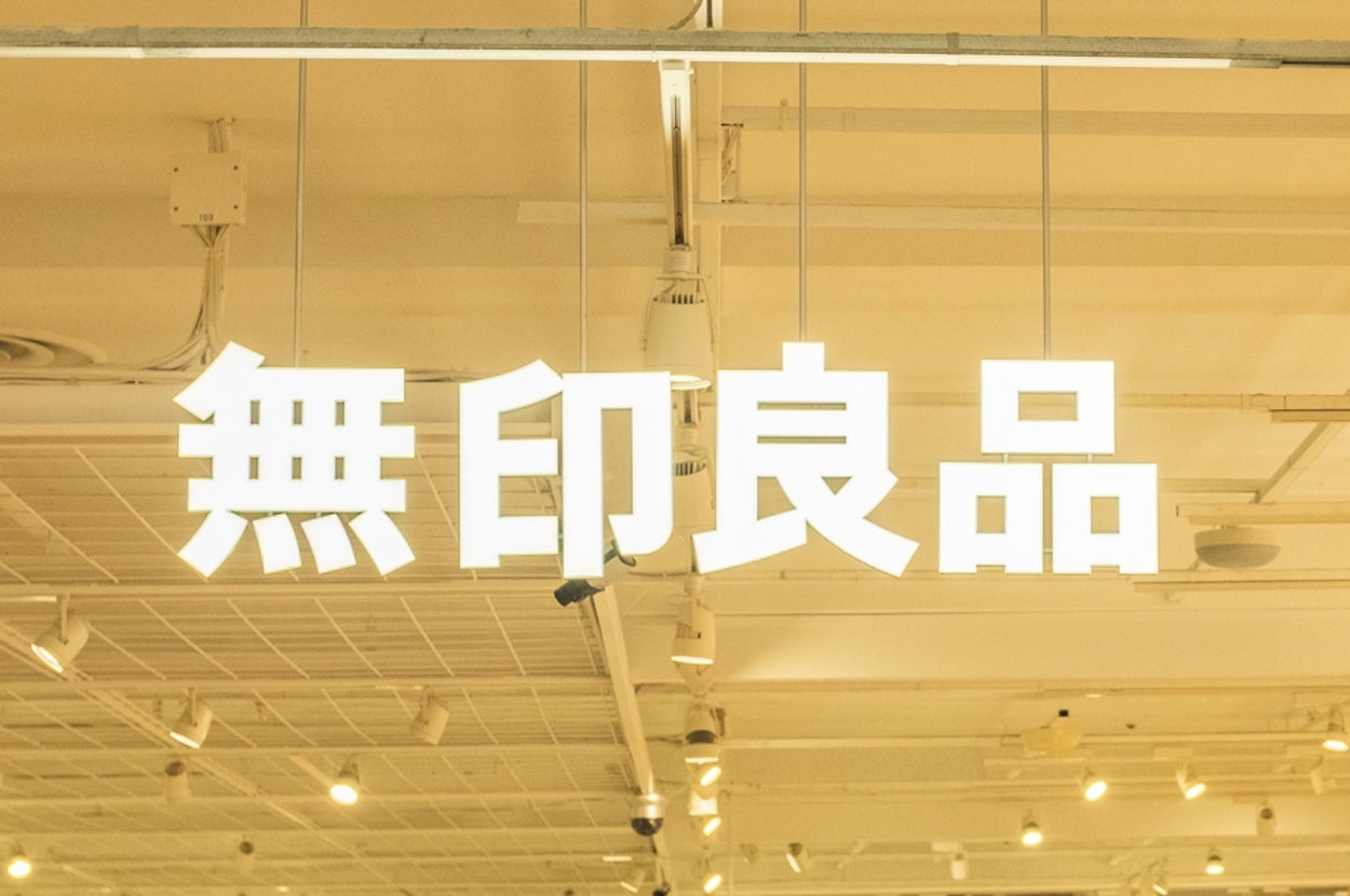 Shoppers browsing inside a spacious, organized store with wooden shelves and various displayed products. Signage with non-English characters hangs above