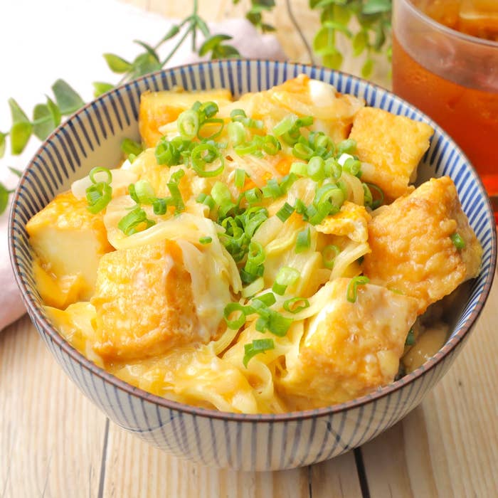 ボウルに入った揚げ豆腐がネギで飾られた料理。背景に冷たい飲み物。