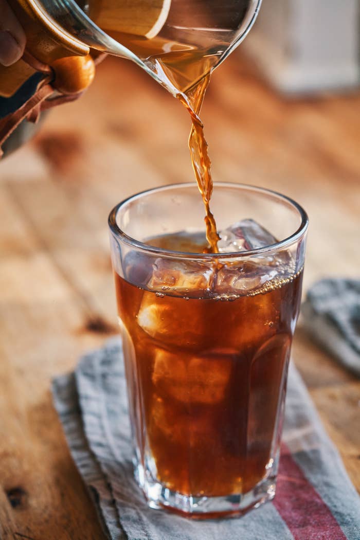 Pouring iced coffee into a glass filled with ice cubes on a wooden table