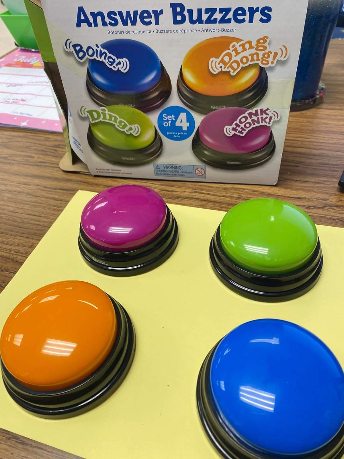 Four colorful answer buzzers on a table with packaging showing sound effects like "Ding!" and "Boing!"