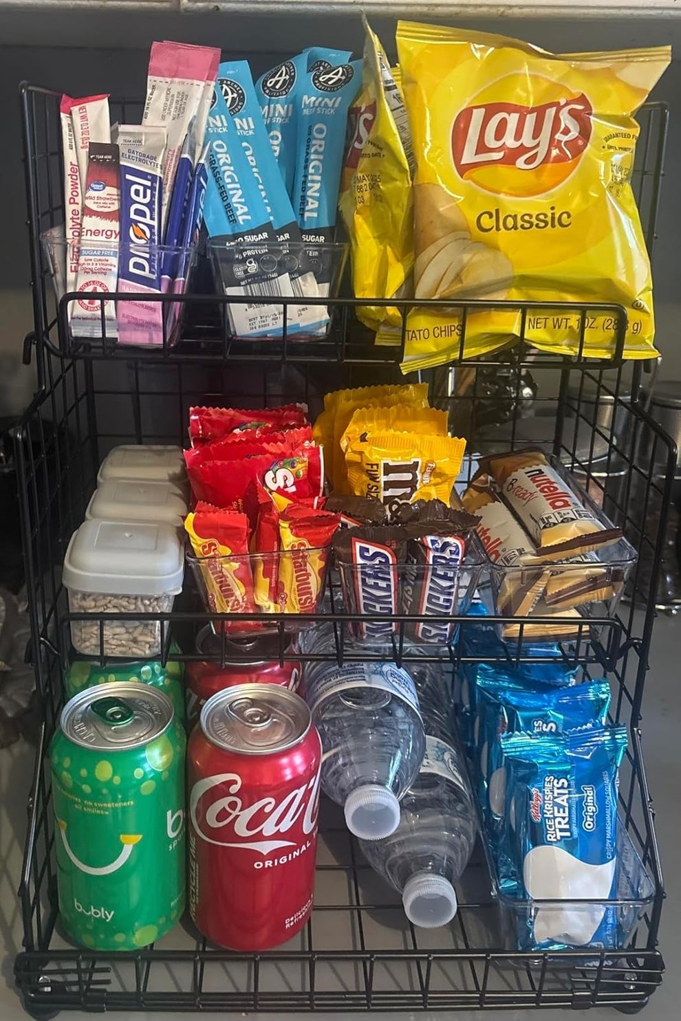 Snack display with chips, candy, granola bars, cereals, beverages, and Rice Krispies Treats organized on a three-tier wire rack