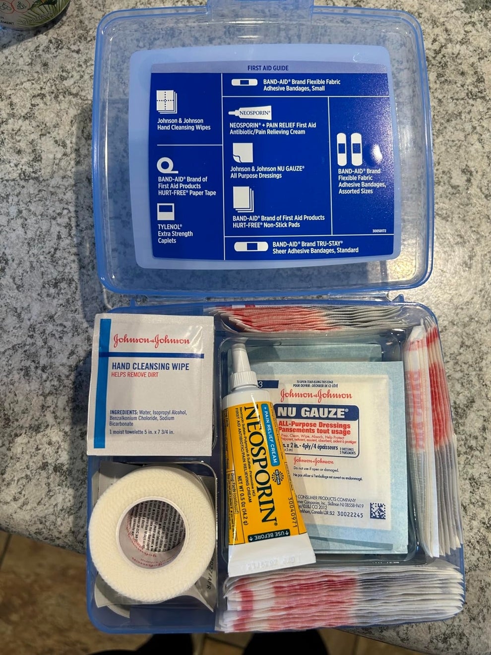 Open first aid kit with bandages, antiseptic wipes, medical tape, gauze pads, and a tube of Neosporin displayed on a countertop