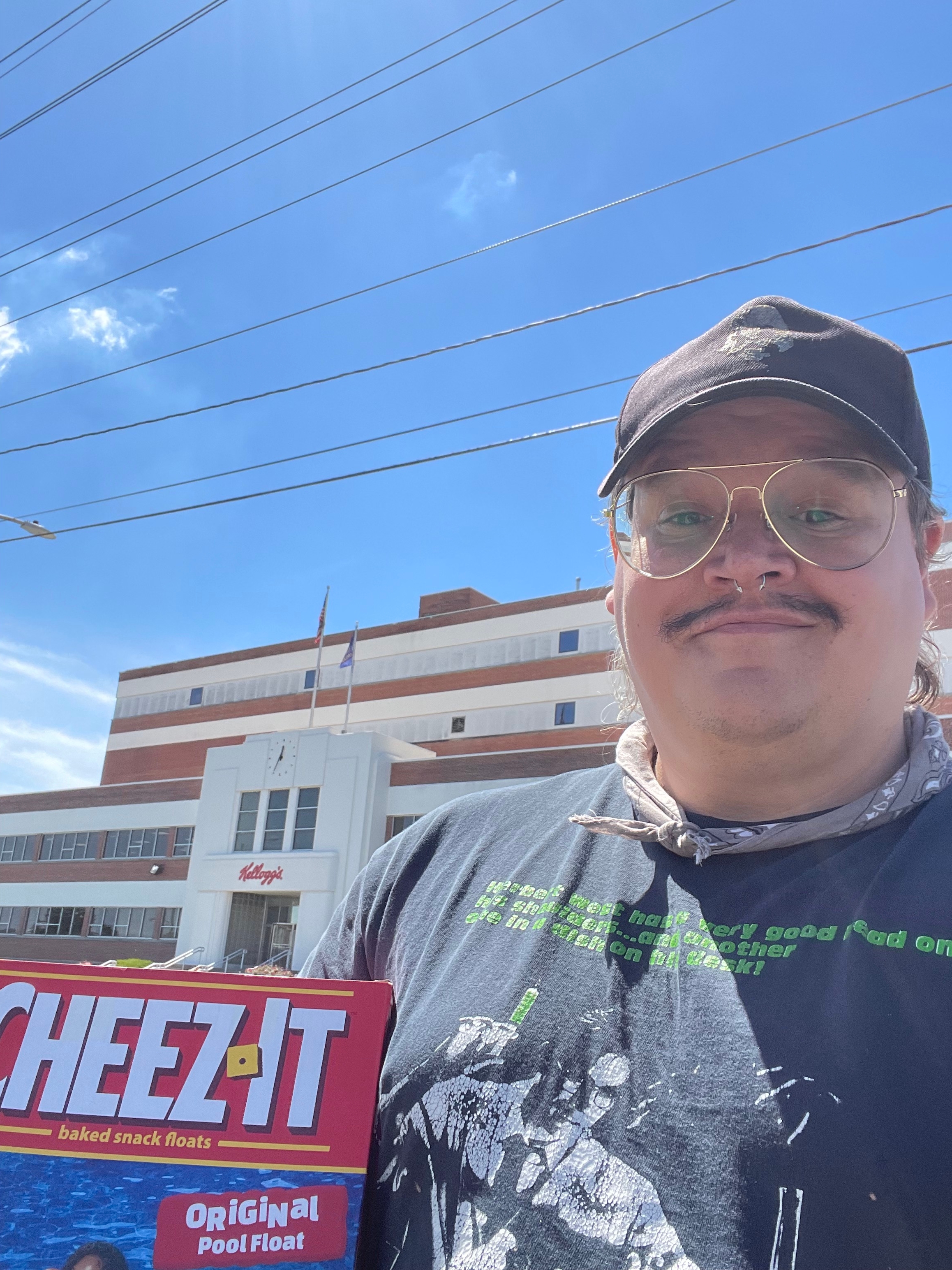 Person outdoors holding a large Cheez-It box in front of the Kellogg's building
