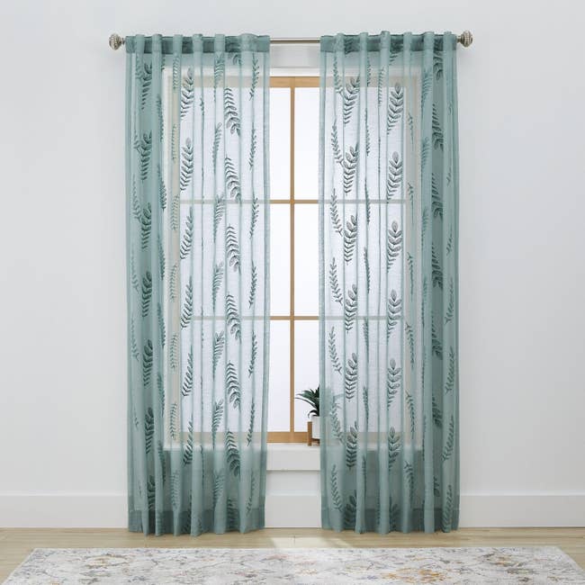 Sheer curtains with leafage patterns bent connected a window.