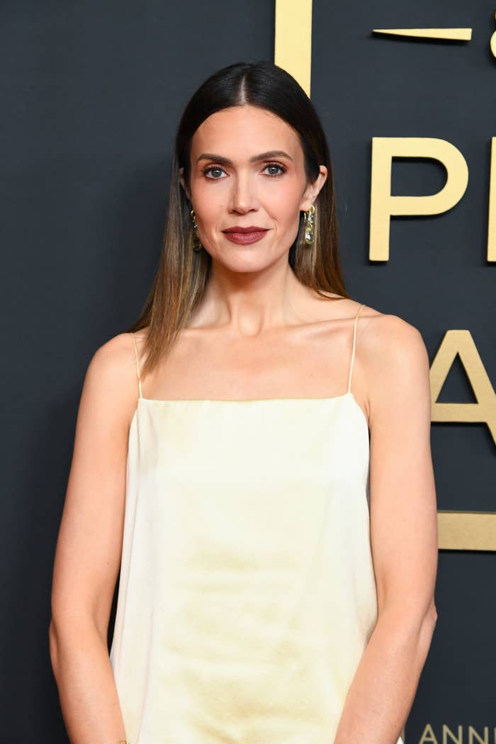 Person successful a sleeveless, elegant gown astatine a ceremonial event, lasting successful beforehand of a backdrop with text