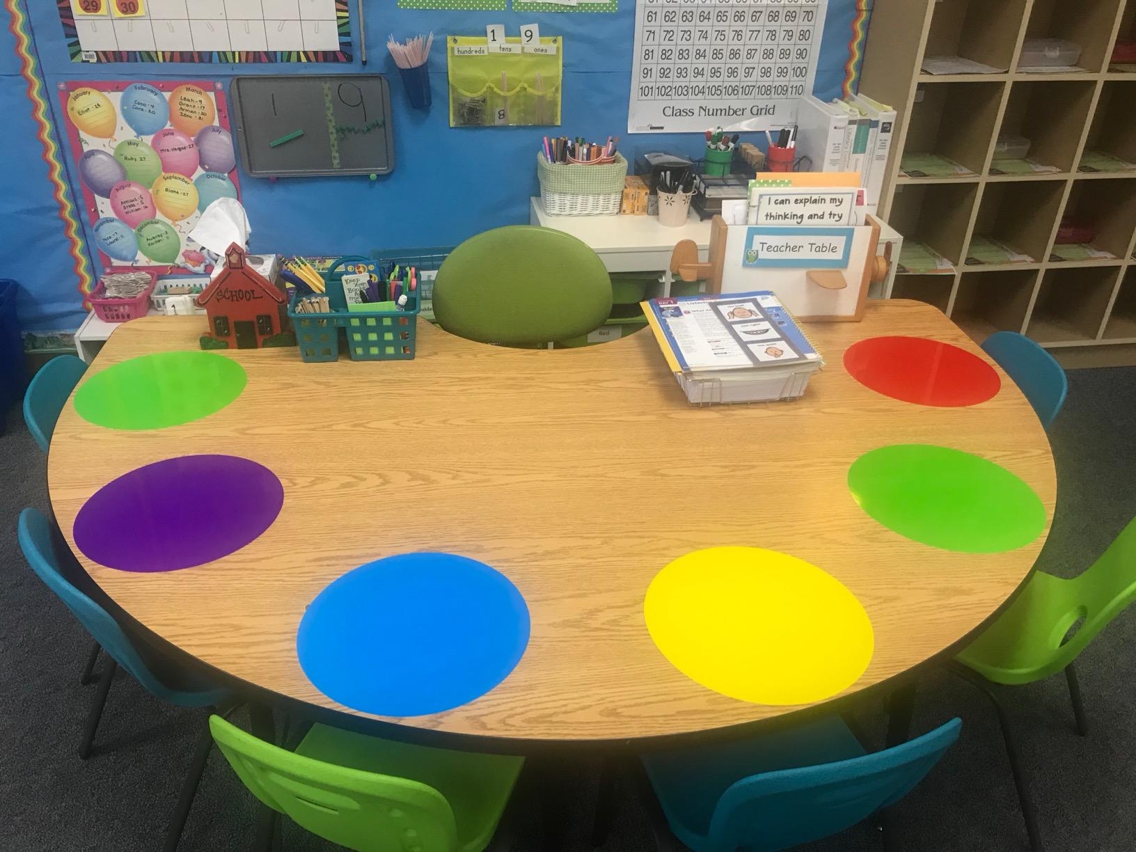 Classroom table with color-coded seating spots for organization. Supplies, a calendar, and educational materials are displayed on and around the table